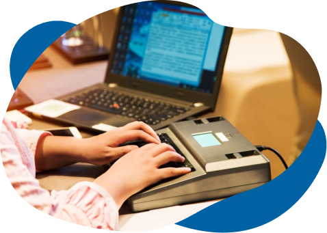 A person using a braille display connected to a laptop, focusing intently on reading or typing, emphasizing accessibility in technology.