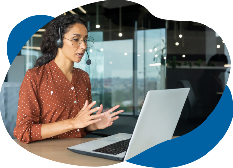 A customer service representative, wearing a headset, communicates animatedly during a video call at her laptop in a modern office setting.